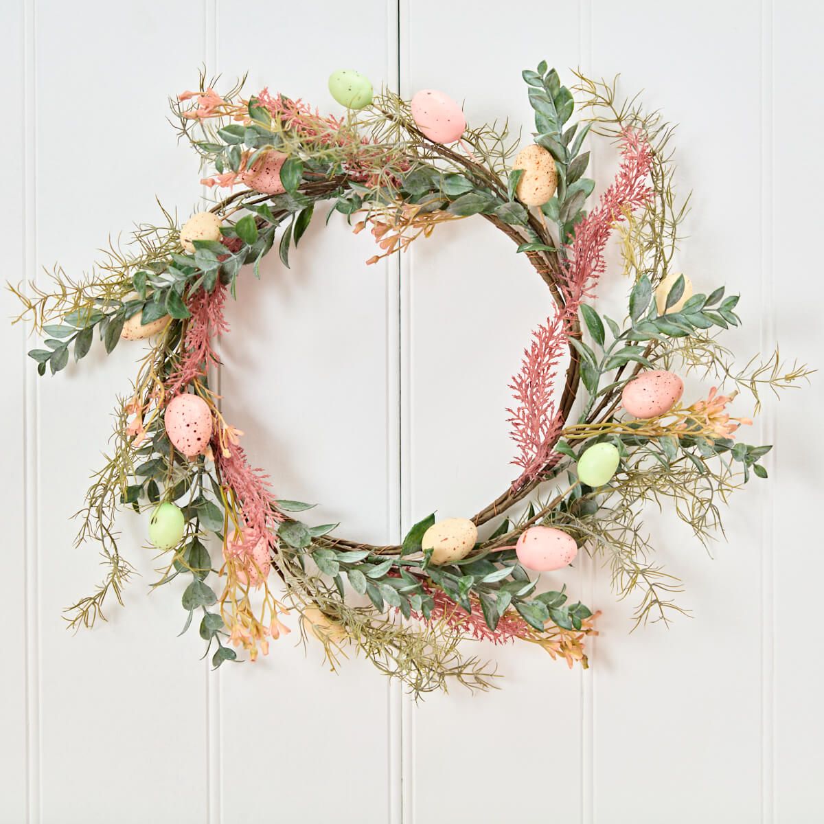 Shabbyquins Easter Egg and foliage spring wreath hanging on wall, decorated with colorful eggs and lush greenery.