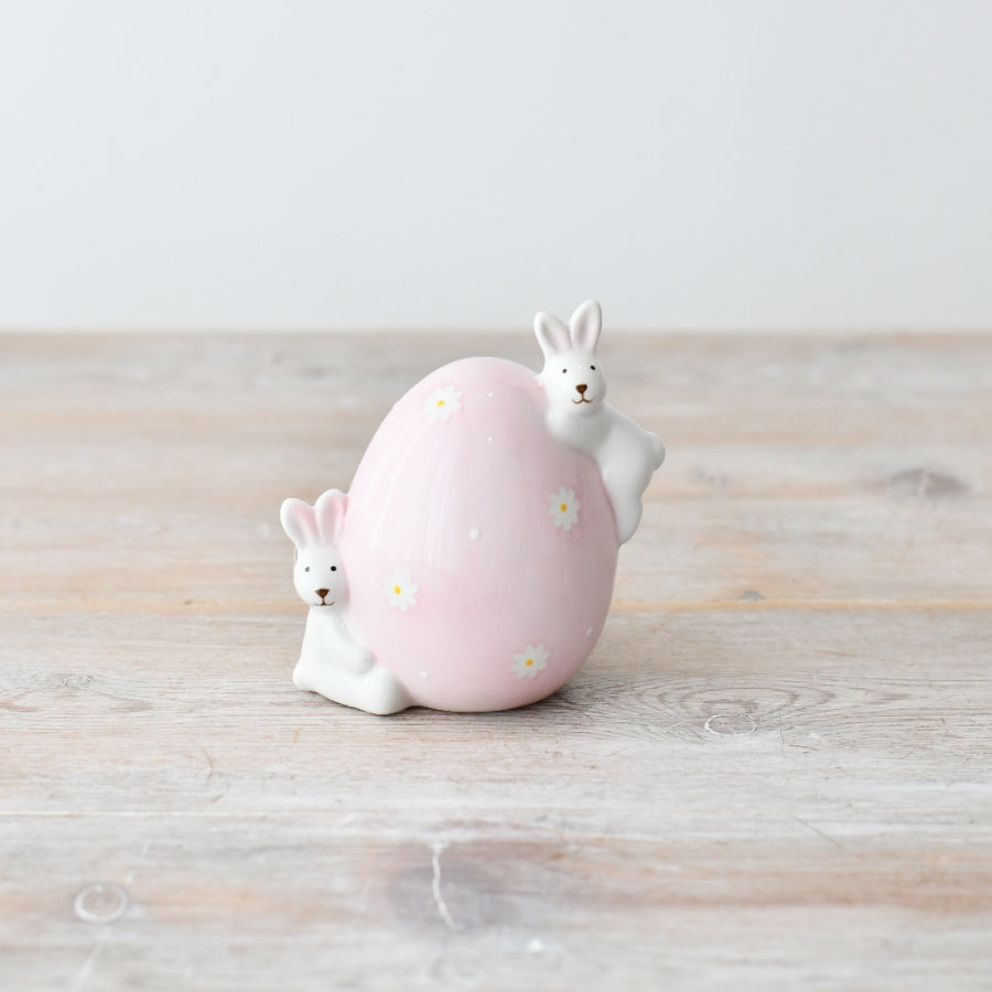 Two ceramic bunny figurines on a seasonal ceramic egg by Sable Homeware, perfect for spring decorations.
