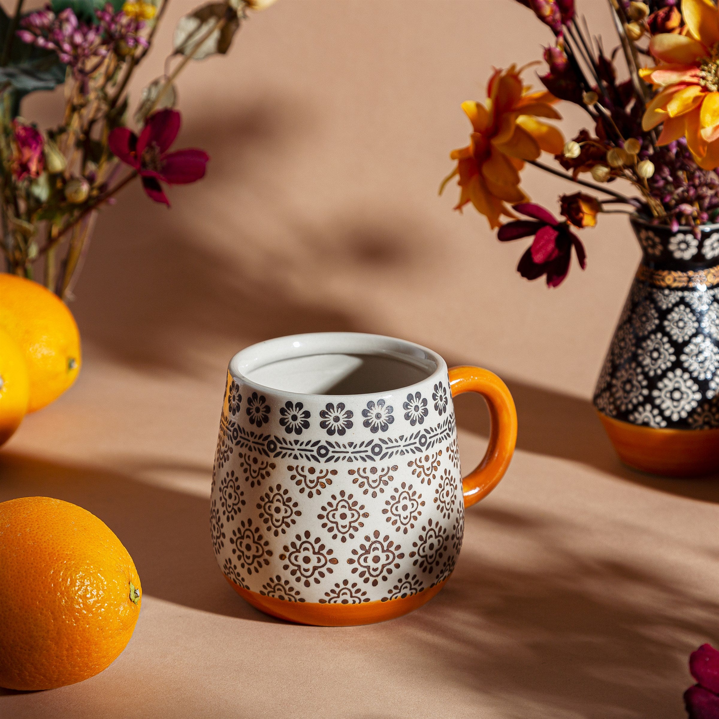 Sable Homeware Anika geometric ceramic mug with black and white pattern, shown on a lifestyle setting with a plant and table